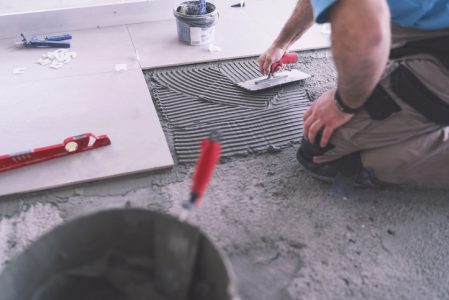 Cropped image of adult builder spreading and smoothing tile adhesive on the floor